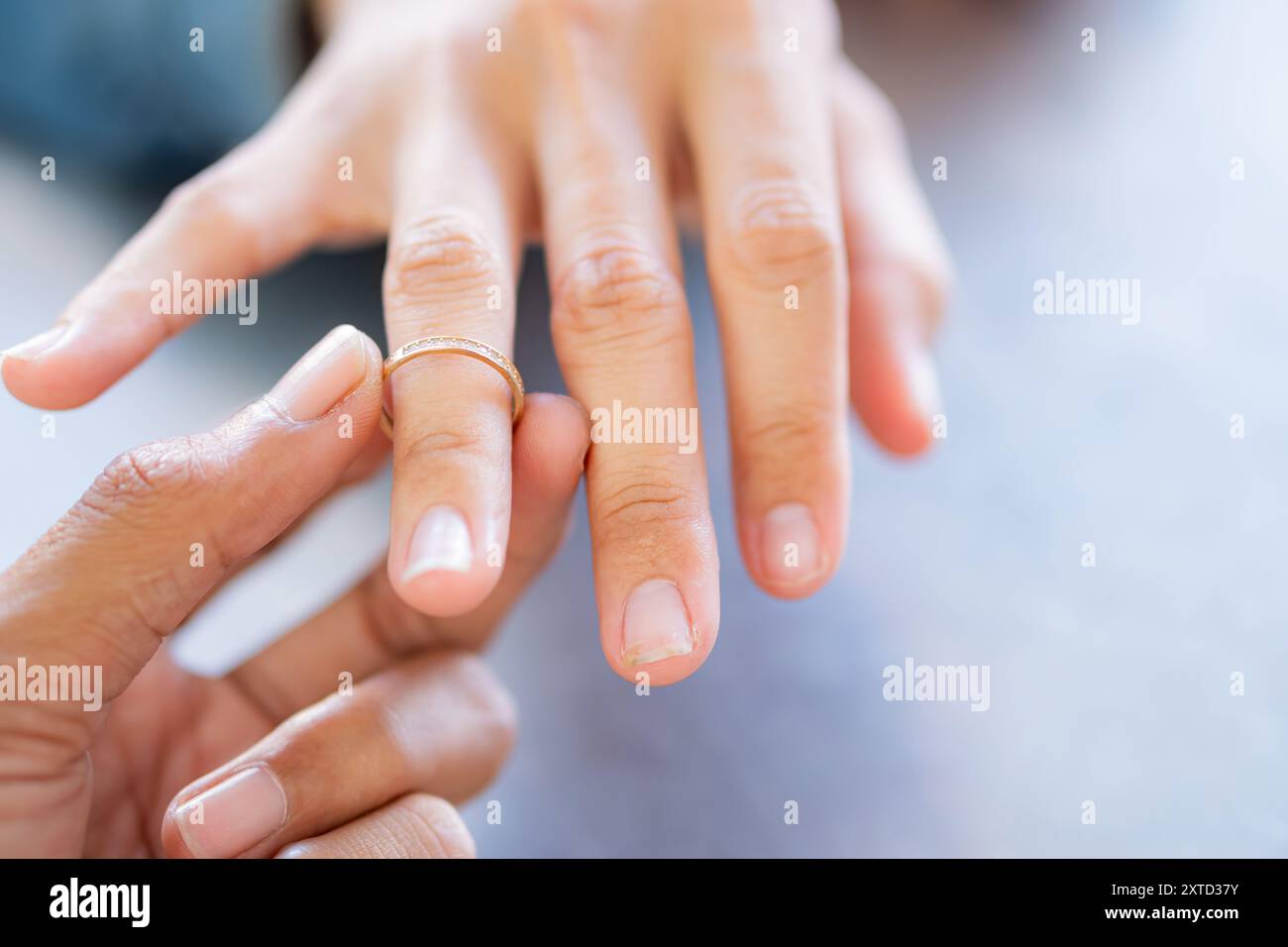 Primo piano di una mano che tiene un anello d'oro, con un'altra mano sullo sfondo. L'attenzione è sull'anello, simboleggiando l'amore o l'impegno. Foto Stock