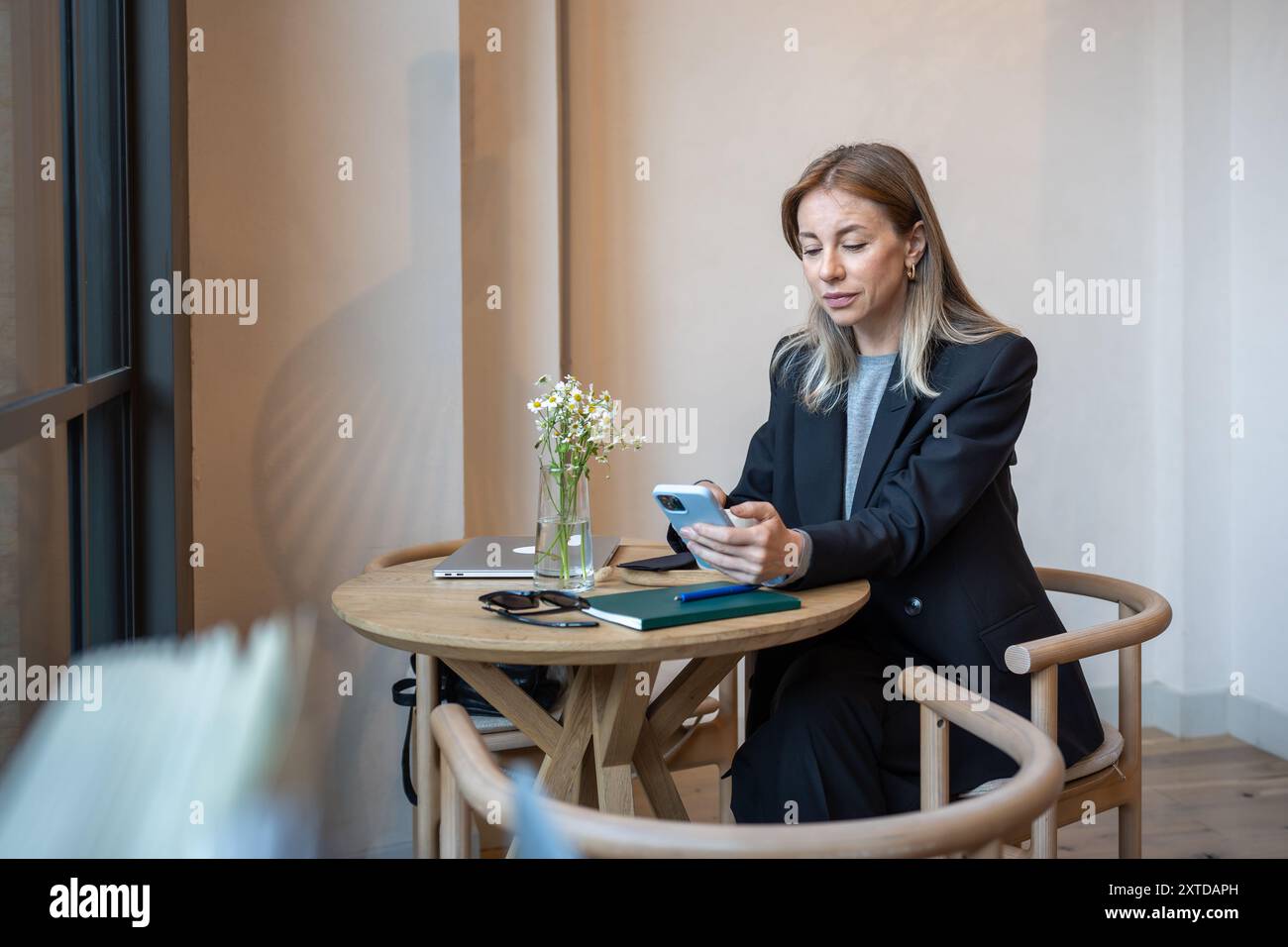 Una donna d'affari interessata al multitasking si rivolge allo smartphone, al laptop in un bar, alla chat e alla gestione online. Foto Stock