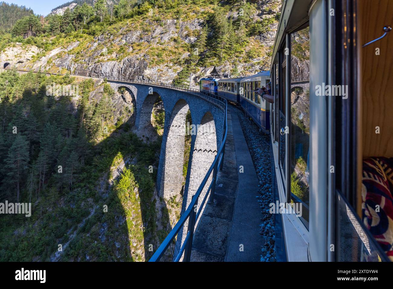 Il viadotto del Landwasser della Ferrovia Retica trasporta l'Alpine Classic Pullman Express attorno a una curva a destra, mentre un passeggero fotografa la scena dal finestrino aperto. Costruito nel 1901/1902, il viadotto a sei arcate è alto 65 metri e lungo 136 metri. Alla sua estremità sud-orientale, la linea porta direttamente nel tunnel del Landwasser. Il treno risale al 1931 e originariamente percorreva la linea come 'Golden Mountain Pullman Express' sulla linea ferroviaria Montreux–Berner Oberland. La Ferrovia Retica lo acquistò nel 1939. Bahnhofplatz, Bergün Filisur, Grigioni, Svizzera. Foto Stock