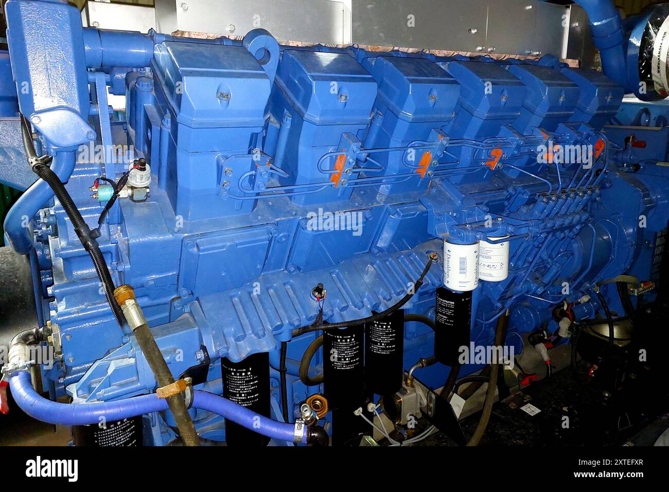 Questo grande motore diesel alimenta un generatore elettrico, mostrandone i componenti e i collegamenti in un ambiente industriale. Foto Stock