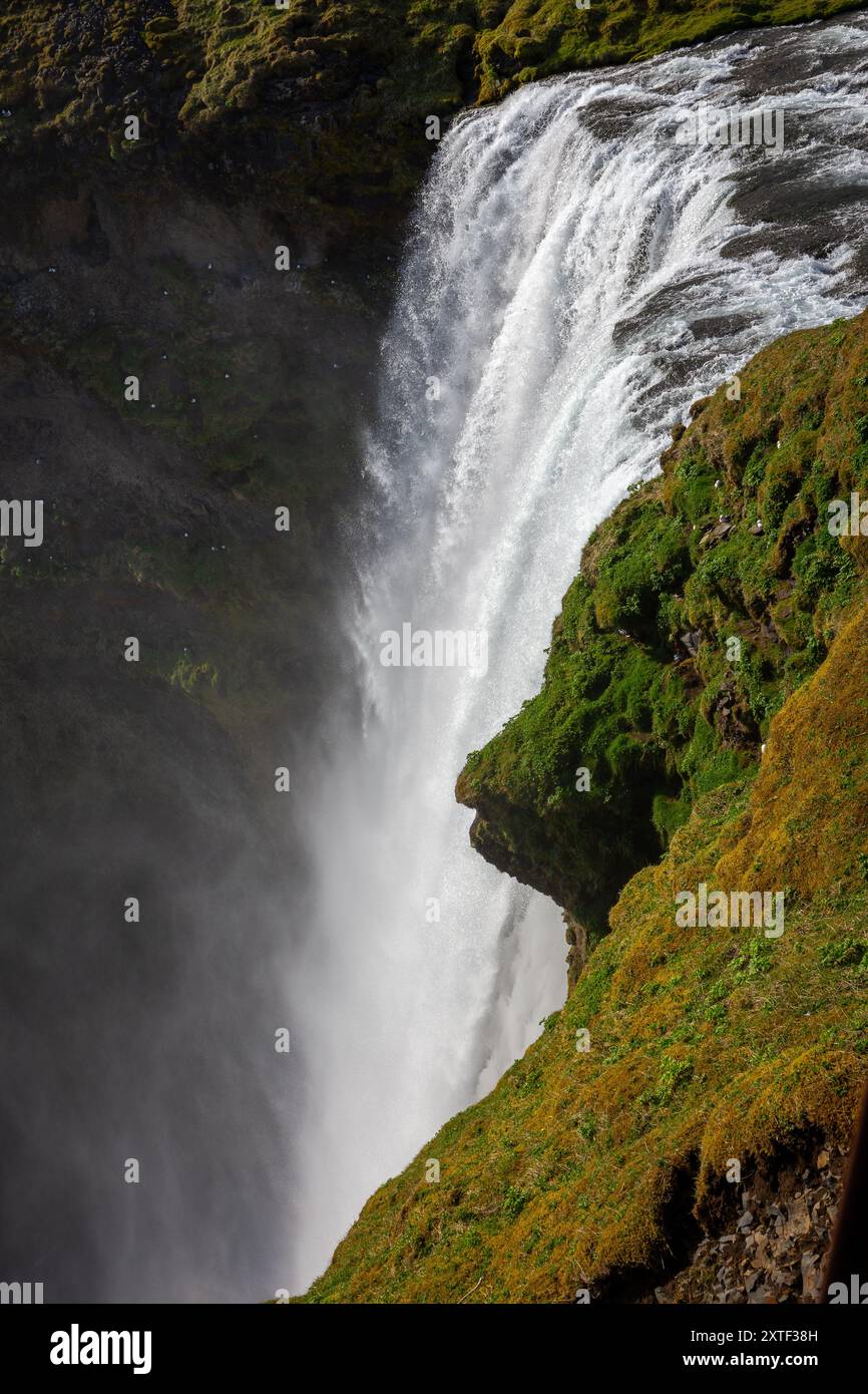 Vista dall'alto della cascata Skogafoss dalla piattaforma di osservazione con spruzzi d'acqua e rocce ricoperte di muschio verde. Foto Stock