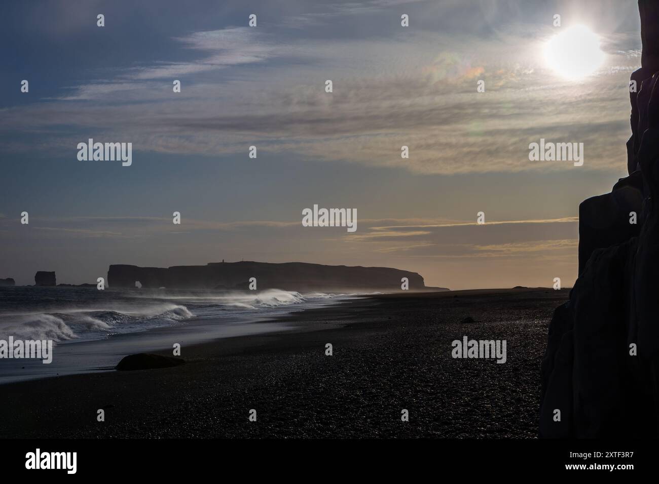 Le onde delle sneaker si infrangono sulla costa di Reynisfjara Black Sand Beach, con forti venti che soffiano acqua e sabbia nera vulcanica, colonne di basalto in primo piano Foto Stock