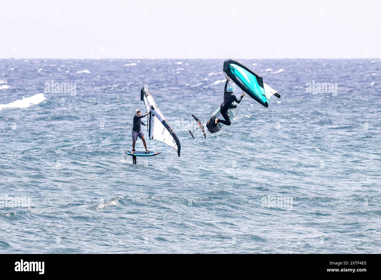 Due atleti che mostrano emozionanti manovre di volo che sventolano sull'oceano a El Medano, Tenerife, Spagna, con onde potenti e cieli limpidi. Foto Stock