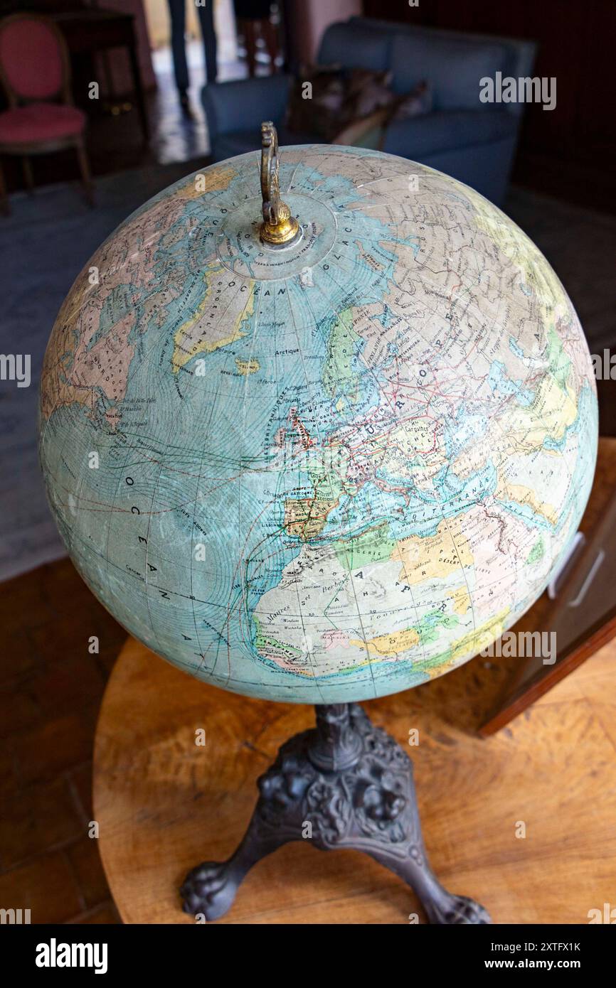 Un antico globo raffigurante la mappa del mondo posizionato su una superficie di legno vicino a una finestra con tende. Foto Stock