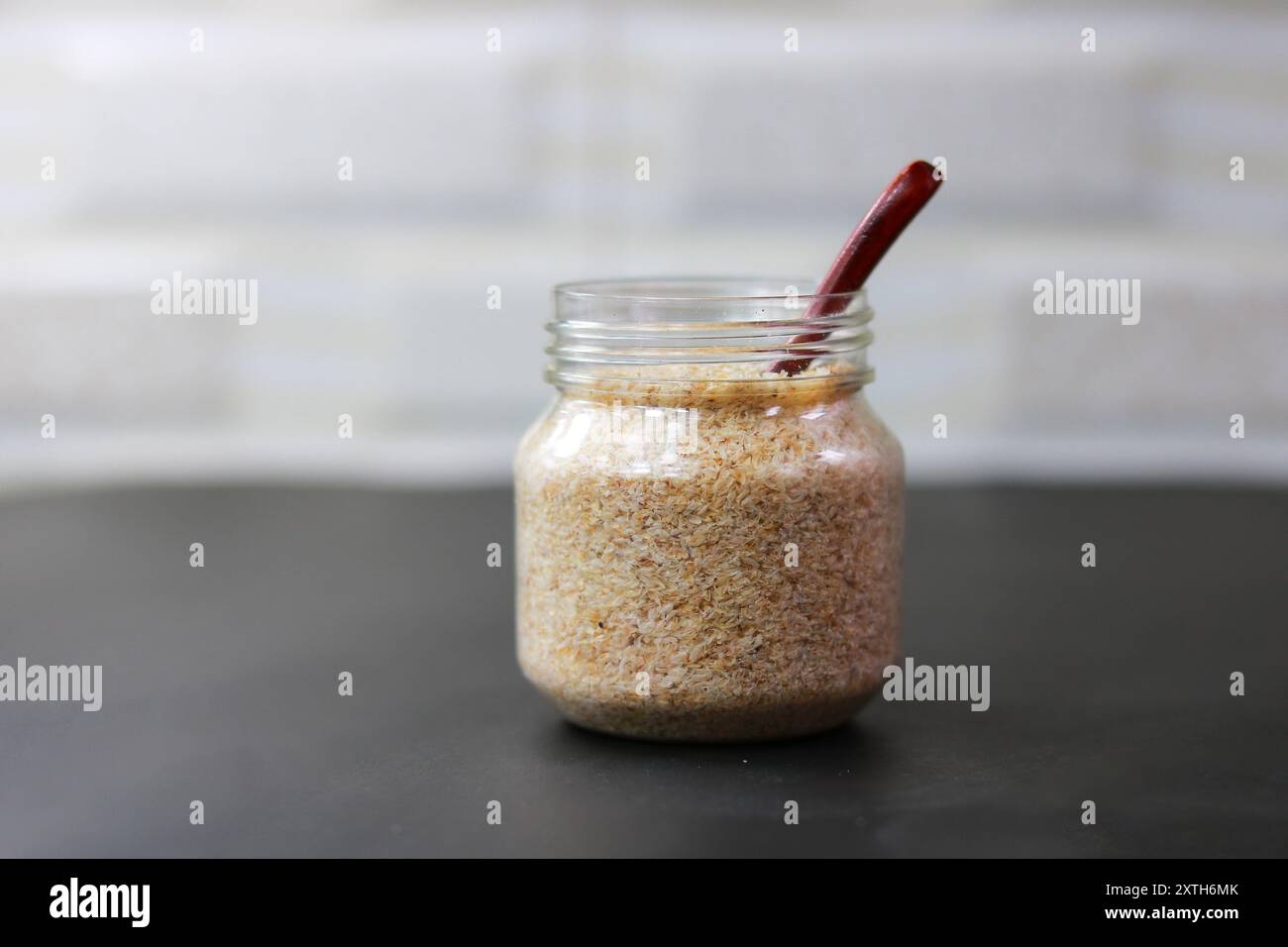 Psyllium Husk (Isabgol) in un vaso di vetro con un cucchiaio di legno su sfondo scuro Foto Stock
