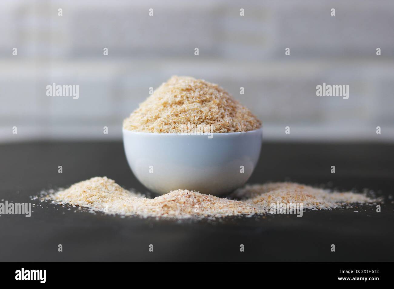 Psyllium Husk (Isabgol) in una ciotola con un cucchiaio di legno su sfondo nero Foto Stock