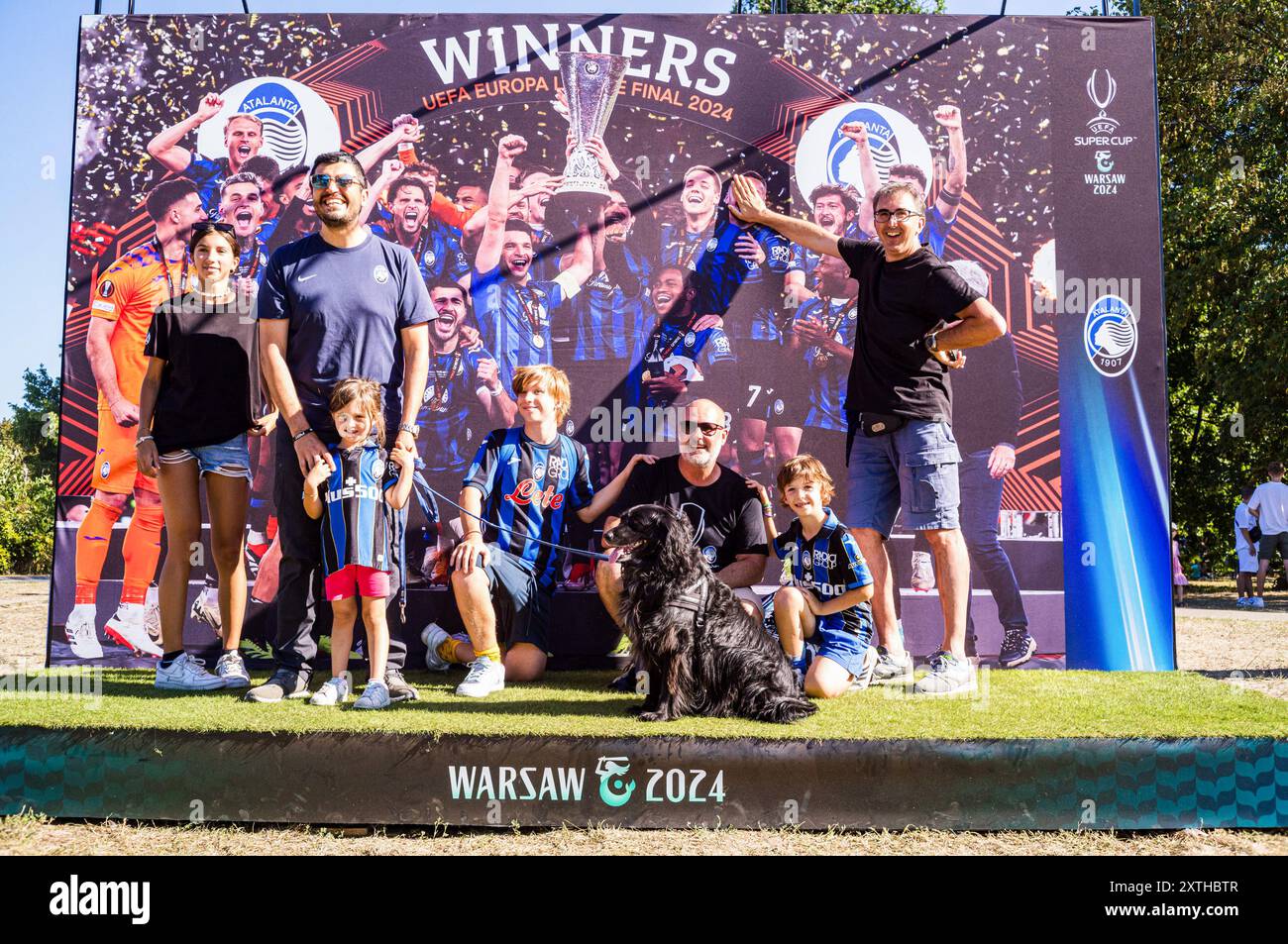 I tifosi dell'Atalanta posano per una foto davanti al banner dei vincitori della UEFA Europa League 2024, i tifosi dei vincitori della Champions League spagnola, del Real Madrid, e dei vincitori della Coppa UEFA italiana, l'Atalanta, riuniti in piazza Kahla a Varsavia, accanto al fiume Vistola, per il festival dei tifosi della Supercoppa UEFA. In previsione della partita di quella sera, i visitatori fanno la fila per scattare foto con il trofeo e partecipare a diverse partite e attività legate al calcio, prima di recarsi allo stadio per la partita. La Supercoppa UEFA si svolge al PGE Narodowy di Varsavia il 14 agosto 2024 ed è contesa dai vincitori di Foto Stock