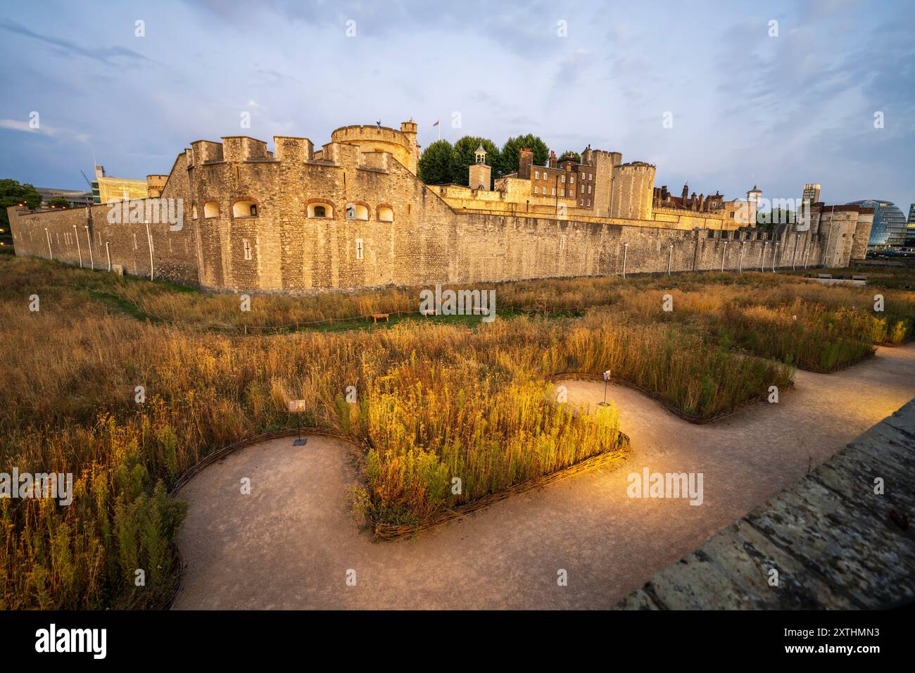 Paesaggio urbano panoramico di Londra con la Torre di Londra, le antiche mura medievali del castello e i giardini del castello con le panchine al tramonto. Niente persone. Foto Stock