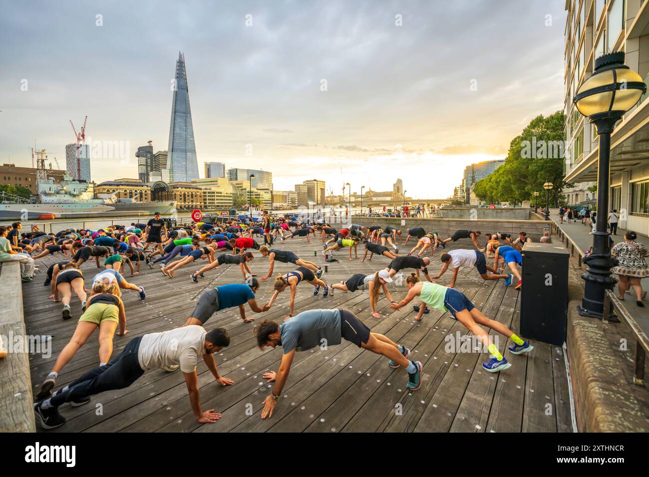 Skyline di Londra con un gruppo di fitness, lezioni di ginnastica all'aperto sulla riva del Tamigi. Panorama urbano di diversi gruppi di persone sane che esercitano Foto Stock