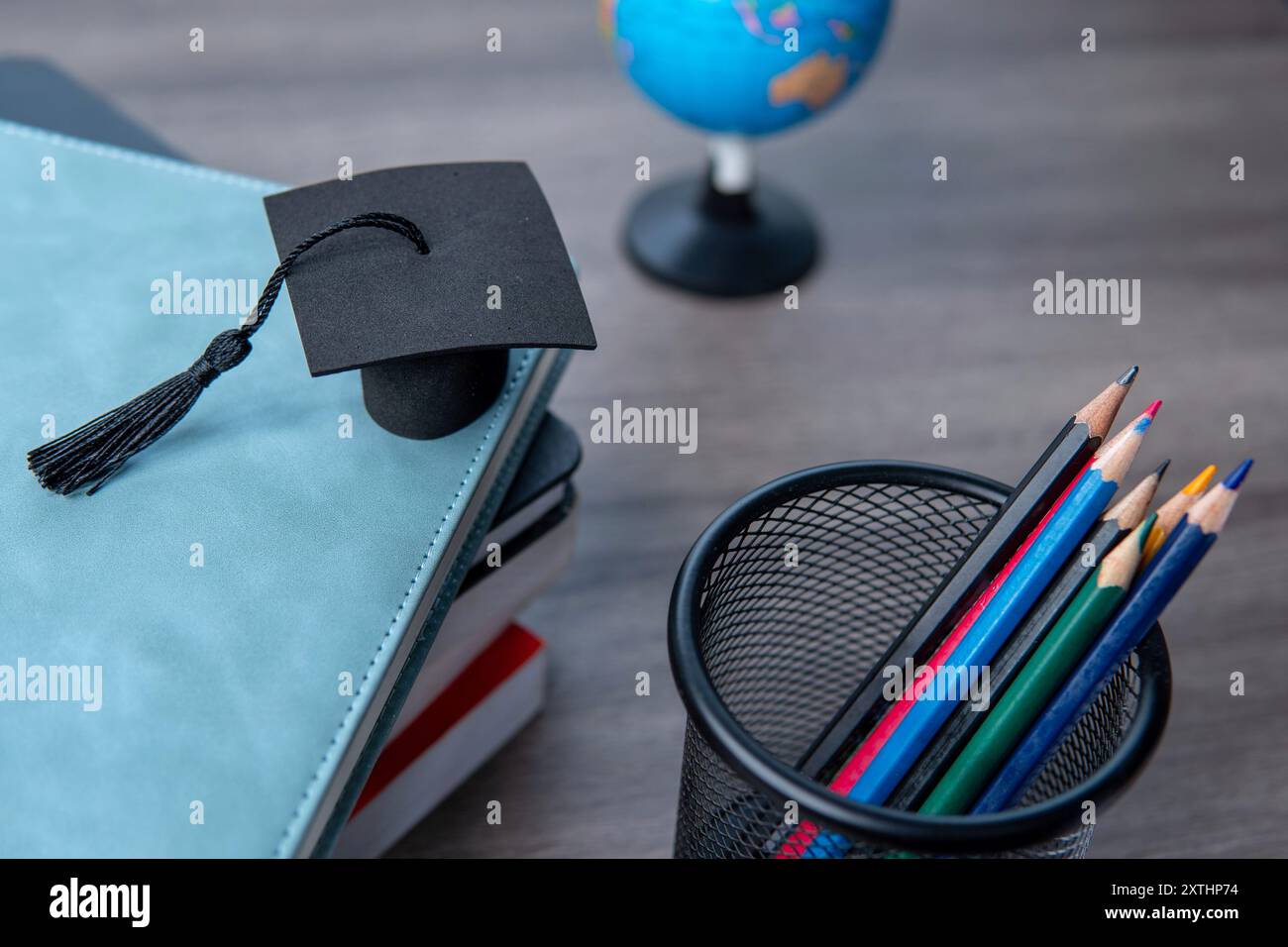 Cappuccio graduato sopra una pila di libri, un globo e una collezione di matite colorate. Concetto di istruzione e apprendimento. Foto Stock