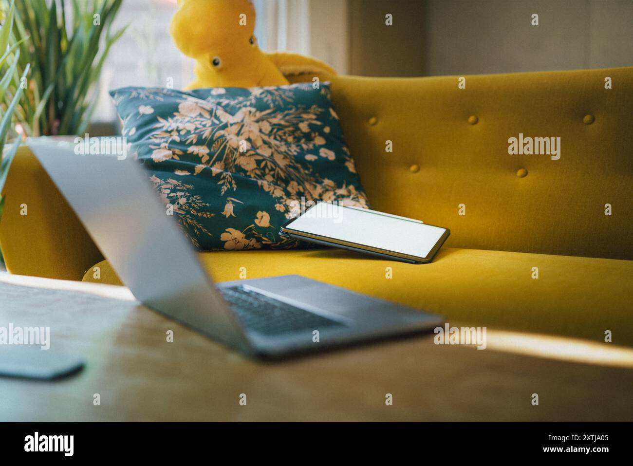 Modello con schermo vuoto del tablet. Comodo divano interno. Aprire il computer portatile su un tavolo di legno. Piante verdi Foto Stock