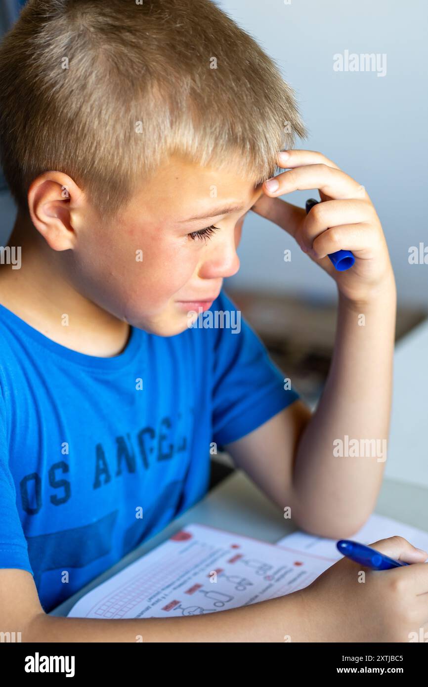 Un ragazzo con una maglietta blu piange per la scuola Foto Stock