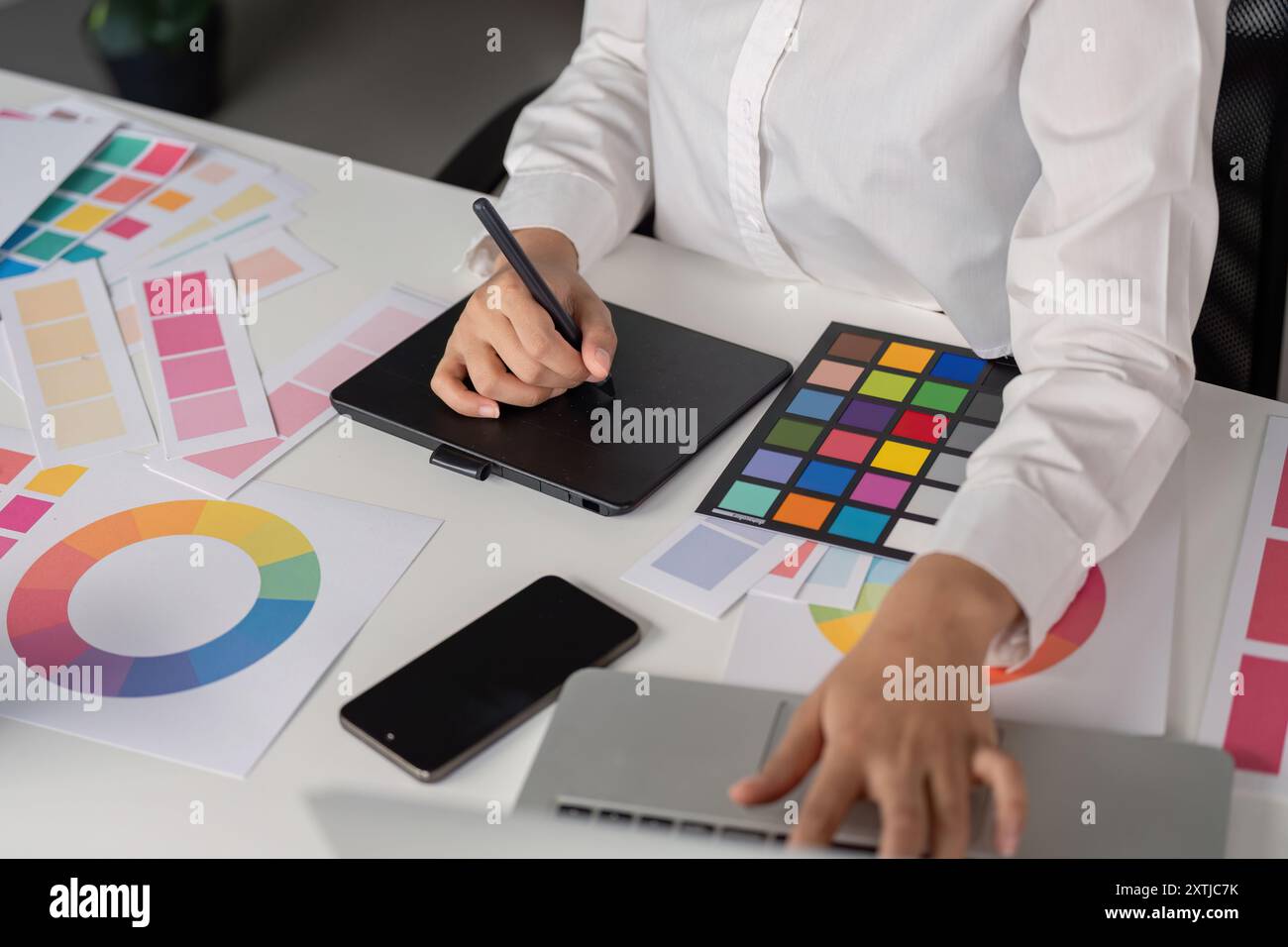 Creative Graphic Designer che lavora con tavolozze colori e tablet digitali in un ambiente d'ufficio moderno Foto Stock