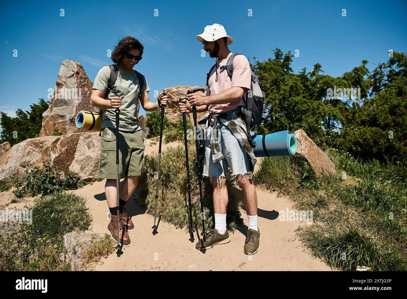Due giovani uomini gay camminano insieme attraverso un paesaggio roccioso e boscoso in una soleggiata giornata estiva. Foto Stock