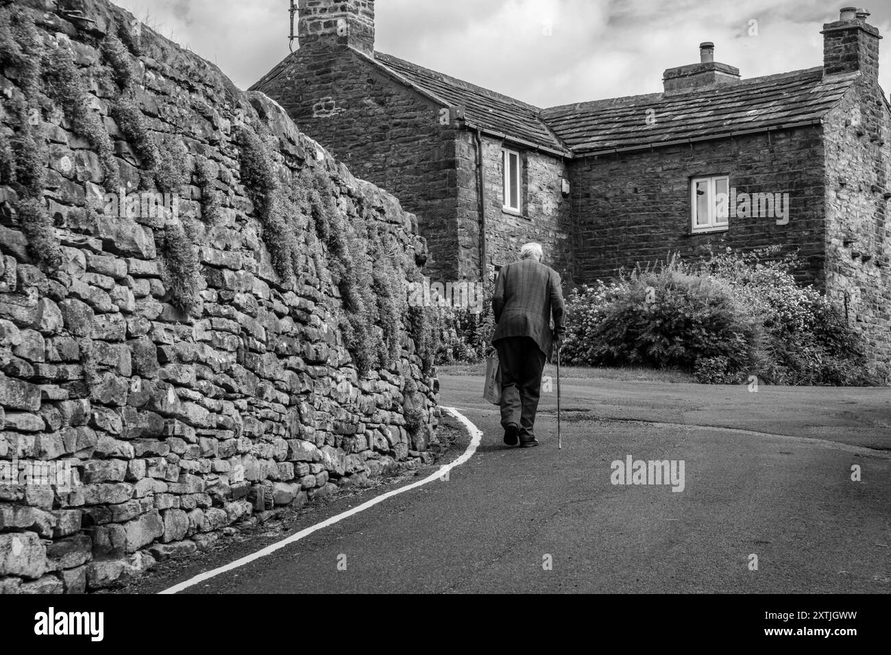 Un vecchio che cammina attraverso il villaggio di Muker, Swaledale, North Yorkshire Foto Stock
