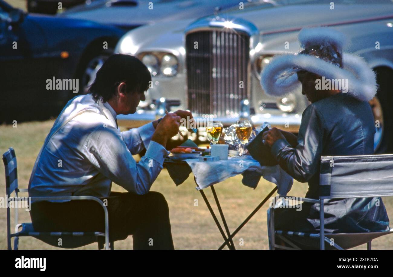 ROYAL ASCOT LADIES DAY retro 1990s vintage elegante coppia di lusso godendo di un picnic all'aperto nei terreni dell'ippodromo Royal Ascot, con la loro auto Bentley sullo sfondo. Ippodromo Royal Ascot, Berkshire. Foto Stock