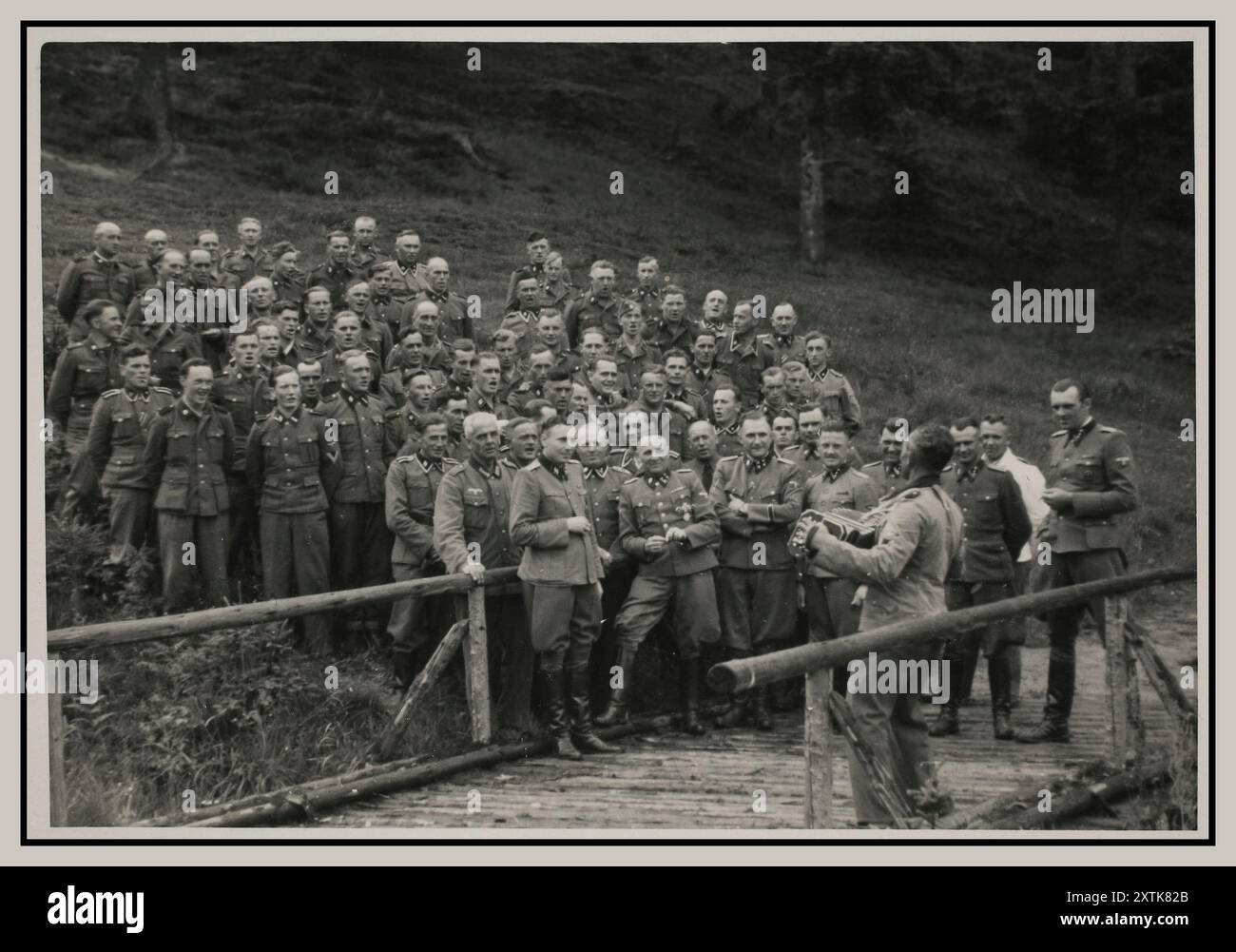 GLI UFFICIALI delle SS DI AUSCHWITZ un fisarmonicista conduce un canto per gli ufficiali delle SS Waffen naziste felici nel loro ritiro a Solahuette fuori Auschwitz. Nella foto in prima fila sono Karl Hoecker, otto Moll, Rudolf Hoess, Richard Baer, Josef Kramer (in piedi leggermente dietro Hoessler e parzialmente oscurato), Franz Hoessler, Josef Mengele e Walter Schmidetzki. Hermann Buch è al centro. Konrad Wiegand, capo della Fahrbereitschaft (piscina per auto e camion), si trova nel mezzo. [Sulla base degli ufficiali in visita a Solahutte, la foto scattata in onore di Rudolf Hoess che completò il suo mandato come capo della guarnigione di Auschwitz Foto Stock