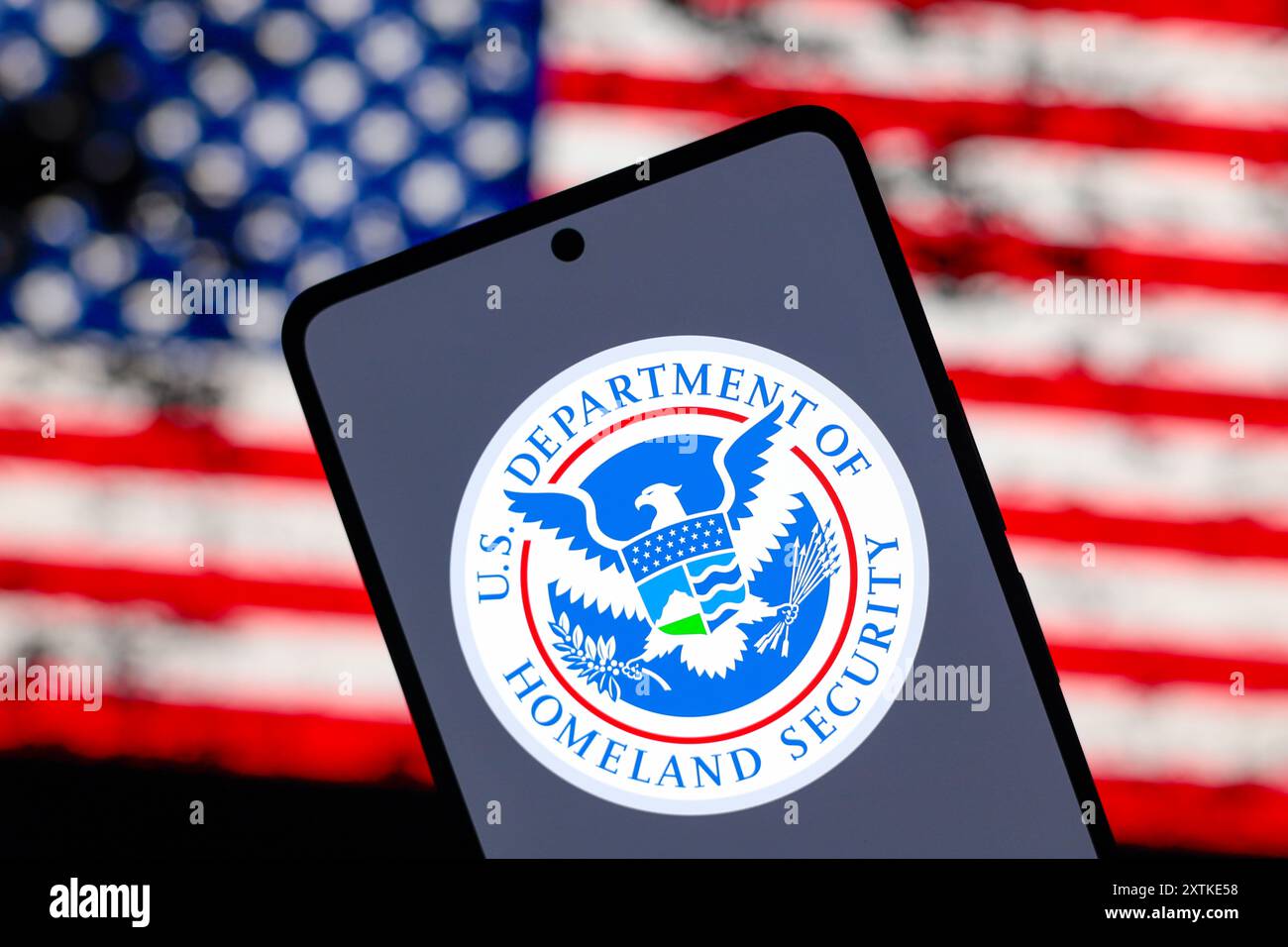 In questa immagine, il logo del Dipartimento per la sicurezza interna degli Stati Uniti (DHS) viene visualizzato sullo schermo di uno smartphone e sullo sfondo la bandiera degli Stati Uniti d'America (USA). Foto Stock