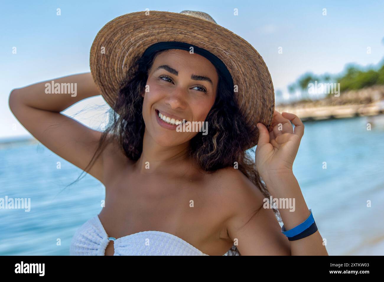 Questa tentatrice tropicale sta vivendo la sua vita migliore nella Riviera Maya. La sua posa sicura e il suo sorriso sensuale, combinati con lo splendido sfondo della spiaggia. Foto Stock
