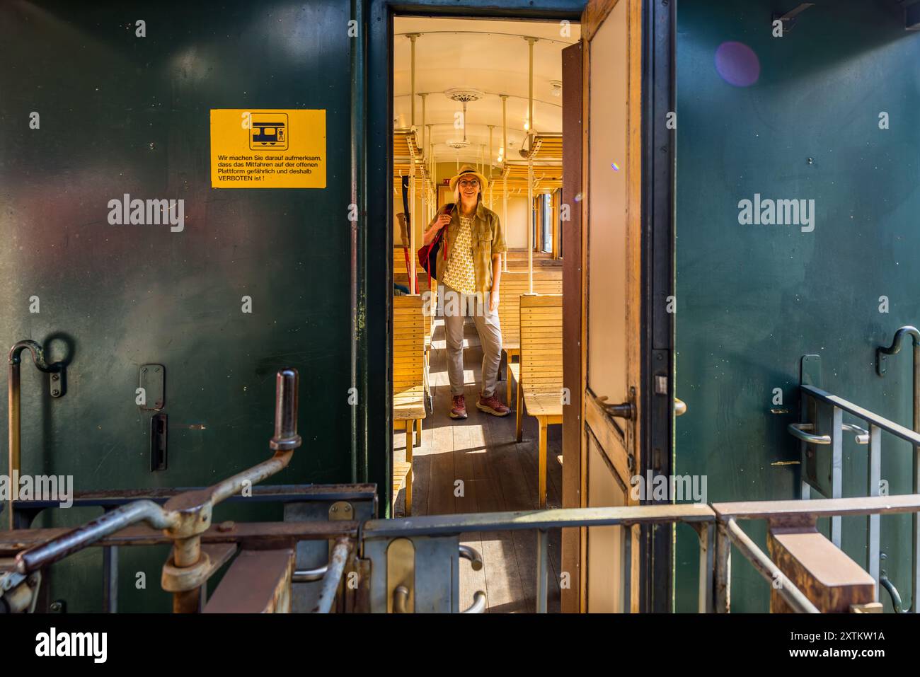 La giornalista Angela Berg attraversa l'interno illuminato dal sole di un vagone storico verde della linea dell'Albula. Un cartello di avvertimento giallo sul muro indica che viaggiare sulla piattaforma aperta è pericoloso e quindi vietato. La Ferrovia Retica gestisce questo viaggio di andata e ritorno Davos Platz–Filisur–Davos Platz con la locomotiva Ge 4/4 I n° 605 'Silvretta', messa in servizio nel 1953, una delle dieci locomotive di questa classe costruite tra il 1947 e il 1953 per la RhB, ognuna chiamata con il nome di una valle o di un paesaggio dei Grigioni. La linea dell'Albula fa parte del Patrimonio mondiale dell'UNESCO 'Ferrovia retica nell'Albul Foto Stock