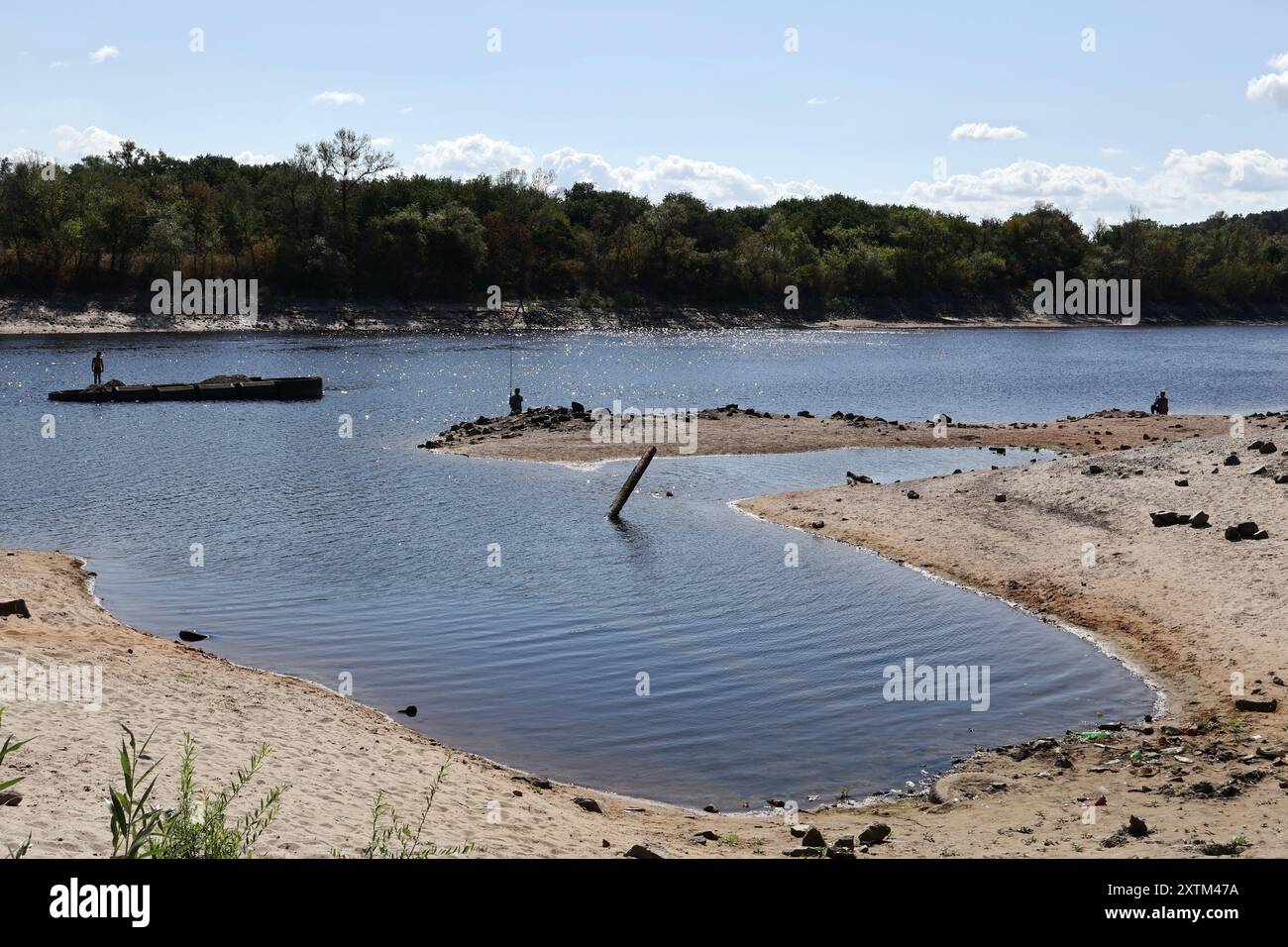 I pescatori visti sulla costa come l'acqua nel fiume Dnipro sono scesi per più di 5,5 metri dopo l'esplosione della diga di Kakhovka. La riva del fiume Dnipro ha iniziato a prosciugarsi ancora una volta (estate 2024). Il livello dell'acqua nel fiume sta diminuendo a causa del calore anomalo e dei problemi legati all'esplosione della diga di Kakhovskaja (giugno 2023). Gli ecologisti sono sicuri che la riduzione dell'acqua nel Dnipro avrà un effetto negativo sui pesci nel serbatoio. Foto Stock