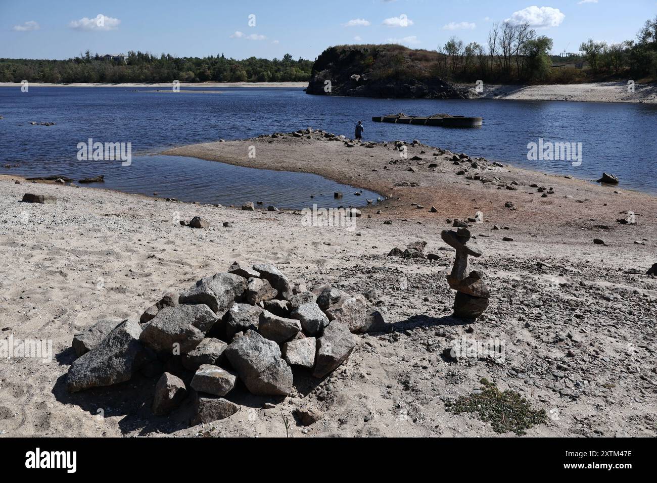 Un pescatore visto sulla costa come l'acqua nel fiume Dnipro è sceso più di 5,5 metri dopo l'esplosione della diga di Kakhovka. La riva del fiume Dnipro ha iniziato a prosciugarsi ancora una volta (estate 2024). Il livello dell'acqua nel fiume sta diminuendo a causa del calore anomalo e dei problemi legati all'esplosione della diga di Kakhovskaja (giugno 2023). Gli ecologisti sono sicuri che la riduzione dell'acqua nel Dnipro avrà un effetto negativo sui pesci nel serbatoio. Foto Stock