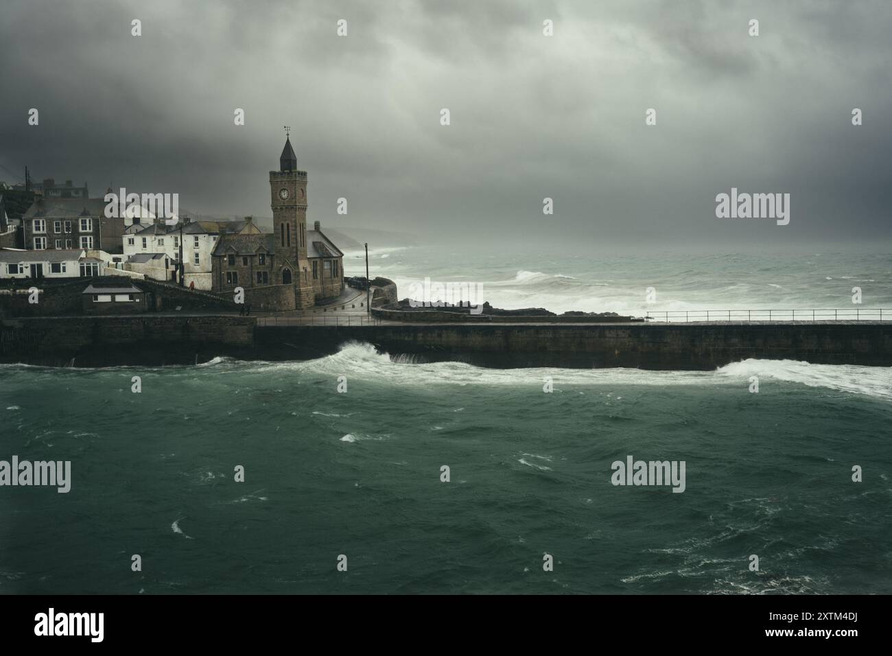Nuvole di tempesta scure con venti di forza e onde che si infrangono contro le mura del porto e la chiesa di Porthleven sulla penisola di Lizard in Cornovaglia Foto Stock
