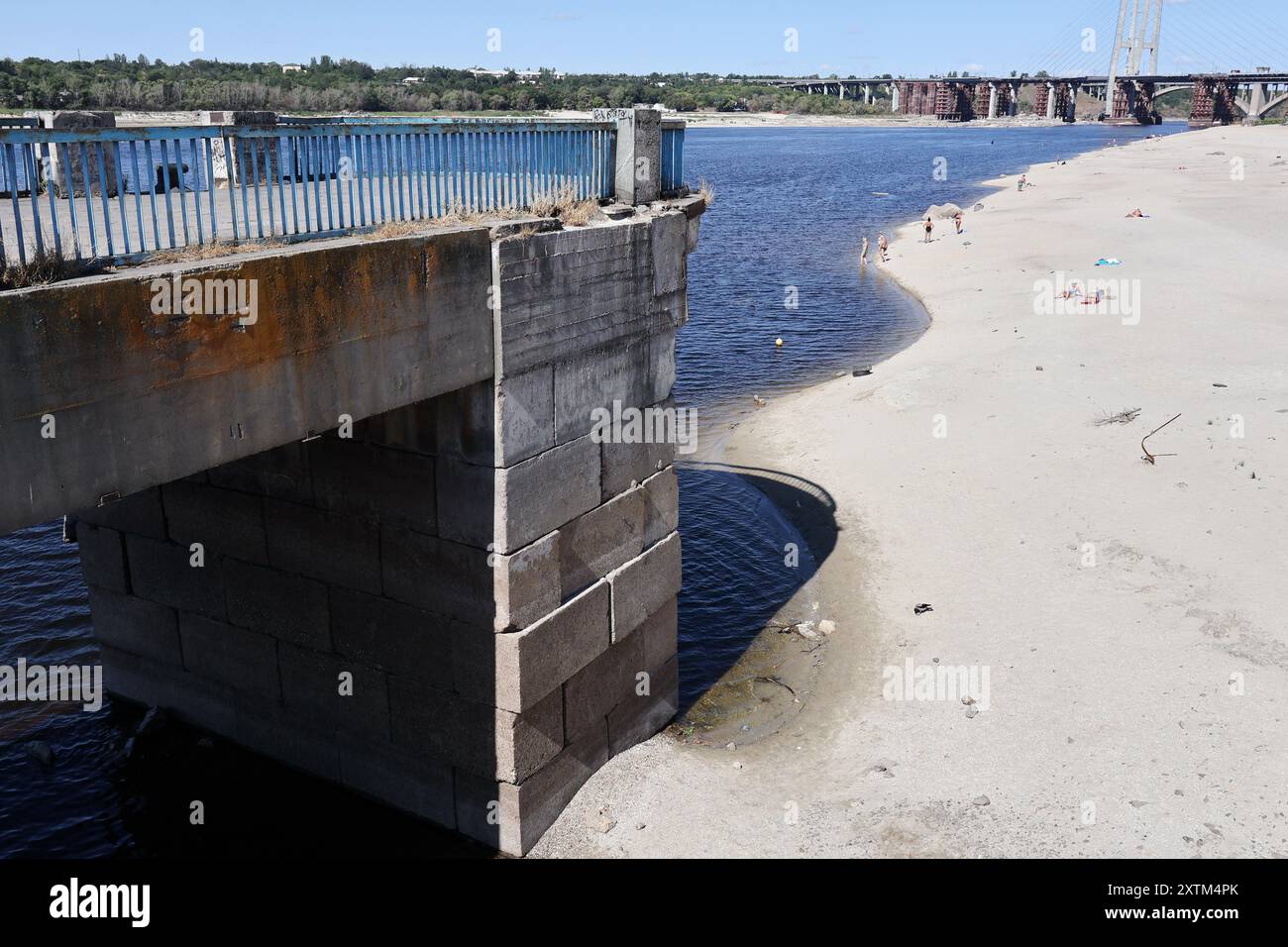 I residenti locali sono visti sul litorale vicino a un molo centrale (a sinistra) mentre l'acqua nel fiume Dnipro è scesa più di 5, 5 metri dopo l'esplosione della diga di Kakhovka. La riva del fiume Dnipro ha iniziato a prosciugarsi ancora una volta (estate 2024). Il livello dell'acqua nel fiume sta diminuendo a causa del calore anomalo e dei problemi legati all'esplosione della diga di Kakhovskaja (giugno 2023). Gli ecologisti sono sicuri che la riduzione dell'acqua nel Dnipro avrà un effetto negativo sui pesci nel serbatoio. (Foto di Andriy Andriyenko/SOPA Images/Sipa USA) Foto Stock