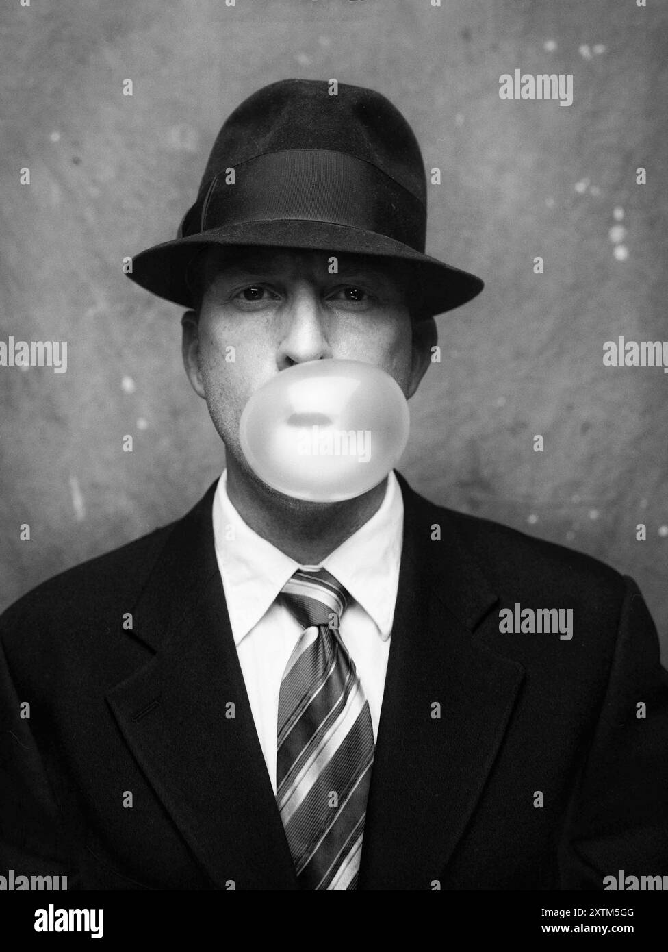 Ritratto a mezza lunghezza di un uomo adulto in tuta e cappello che soffia una bolla di gomma Foto Stock