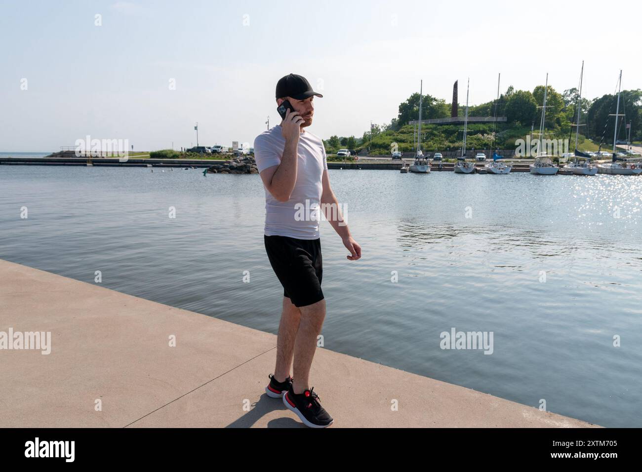 Un giovane con un berretto parla su uno smartphone in riva al lago Foto Stock