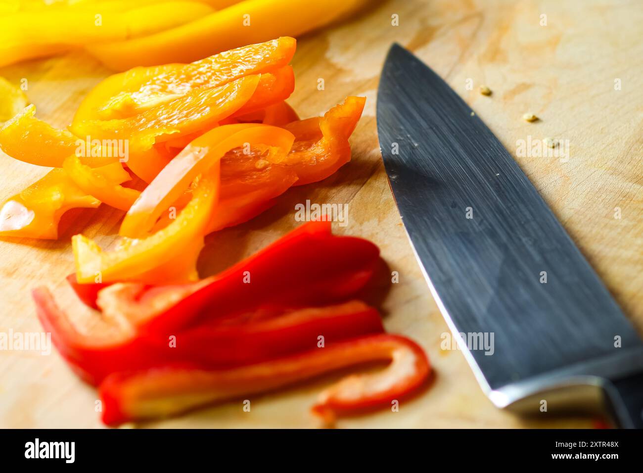 Peperoni tagliati a fette su tagliere in legno con coltello Foto Stock