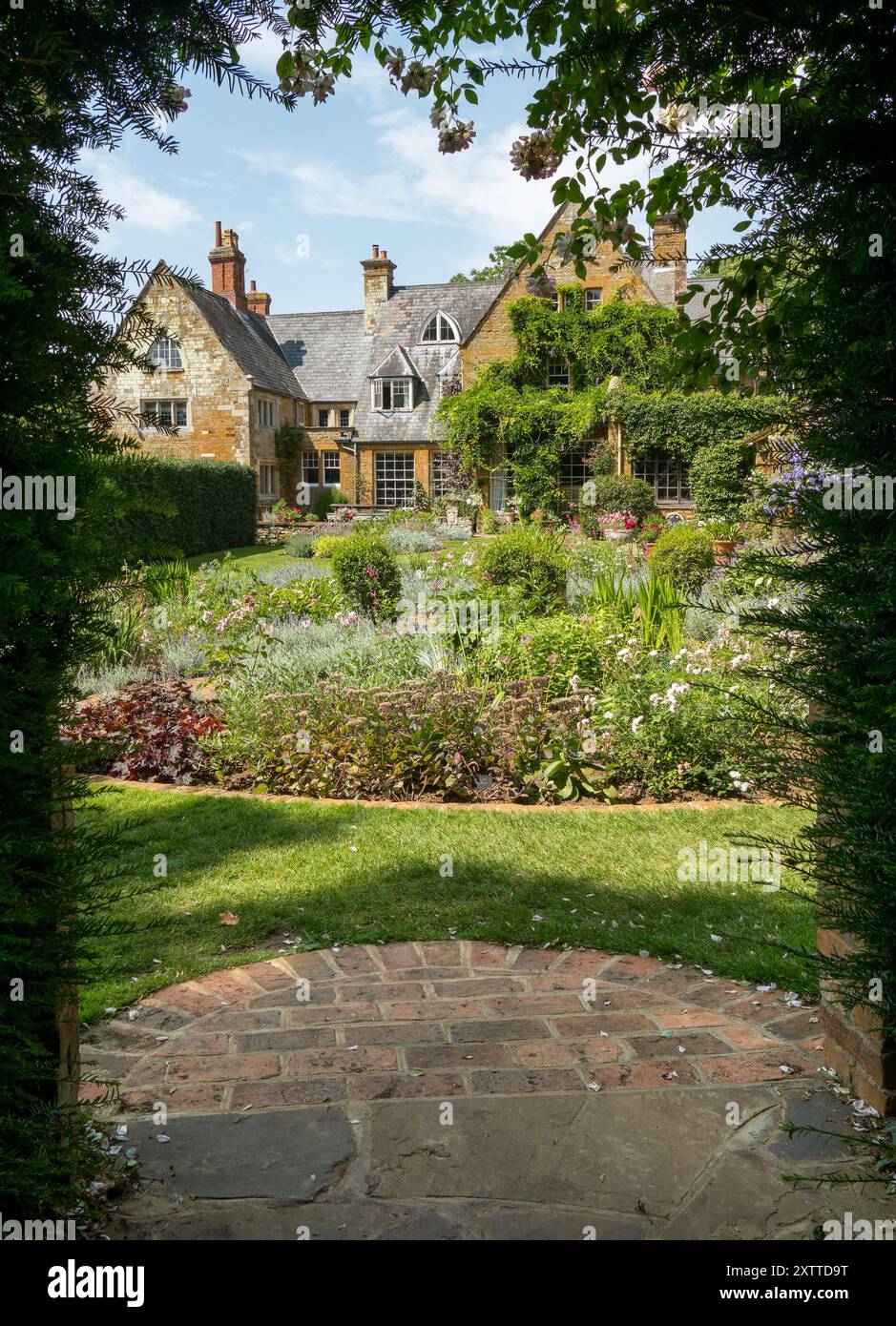 Vista della Coton Manor House and Gardens incorniciata da un arco di siepe di tasso in estate, Northamptonshire, Inghilterra, Regno Unito Foto Stock