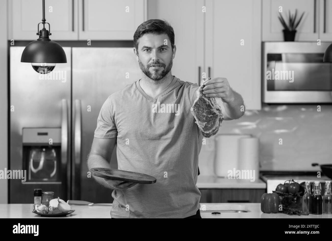 Bell'uomo che cucina carne di manzo in cucina. Ritratto di uomo informale che cucina con ingredienti a base di carne. Uomo informale che prepara carne cruda in cucina. Chef Foto Stock