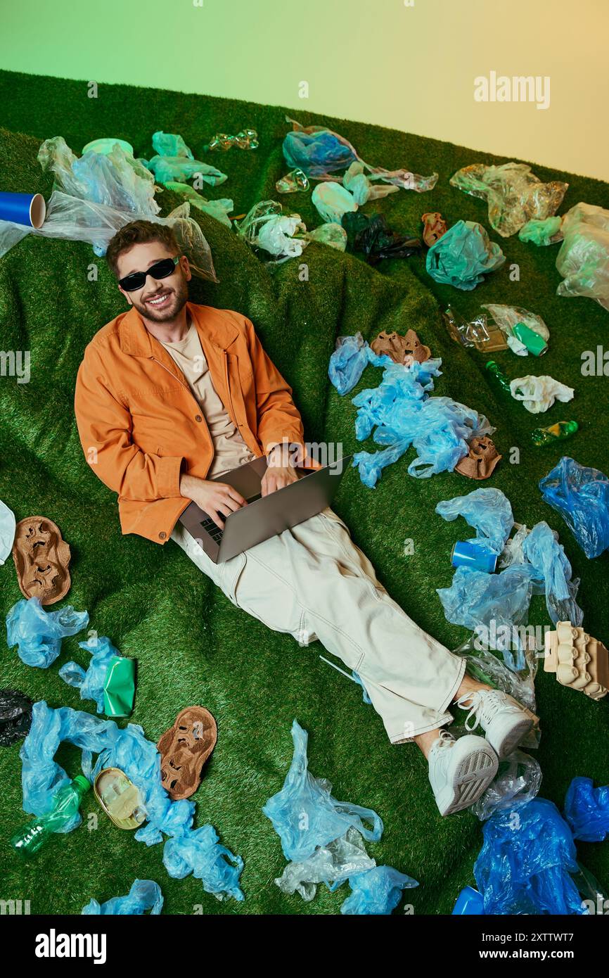 Un uomo sdraiato su un letto di plastica, circondato da una vibrante gamma di oggetti scartati. Foto Stock