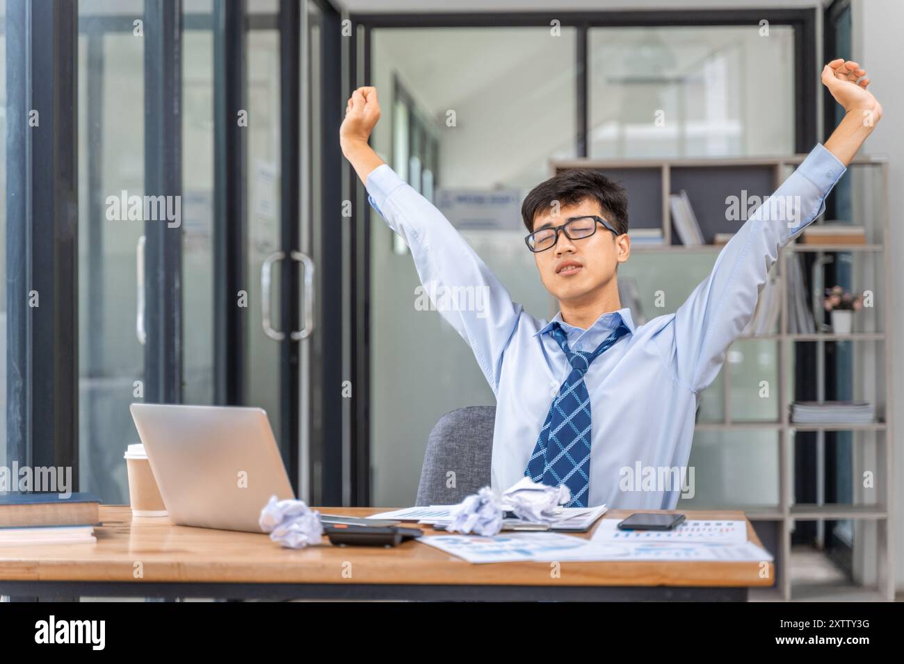 Giovane uomo d'affari stanco e sovraccaricato che si allunga le braccia in stanchezza mentre lavora fino a tardi in ufficio Foto Stock