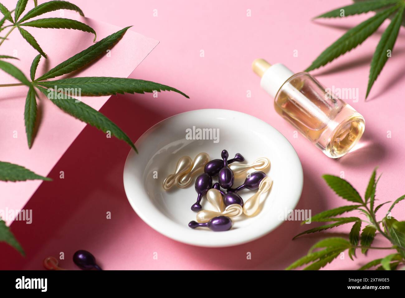 Foglie di marijuana su sfondo rosa chiaro. Con olio essenziale di cannabis e capsule per capelli sani. Marijuana per scopi medici e cosmetici Foto Stock
