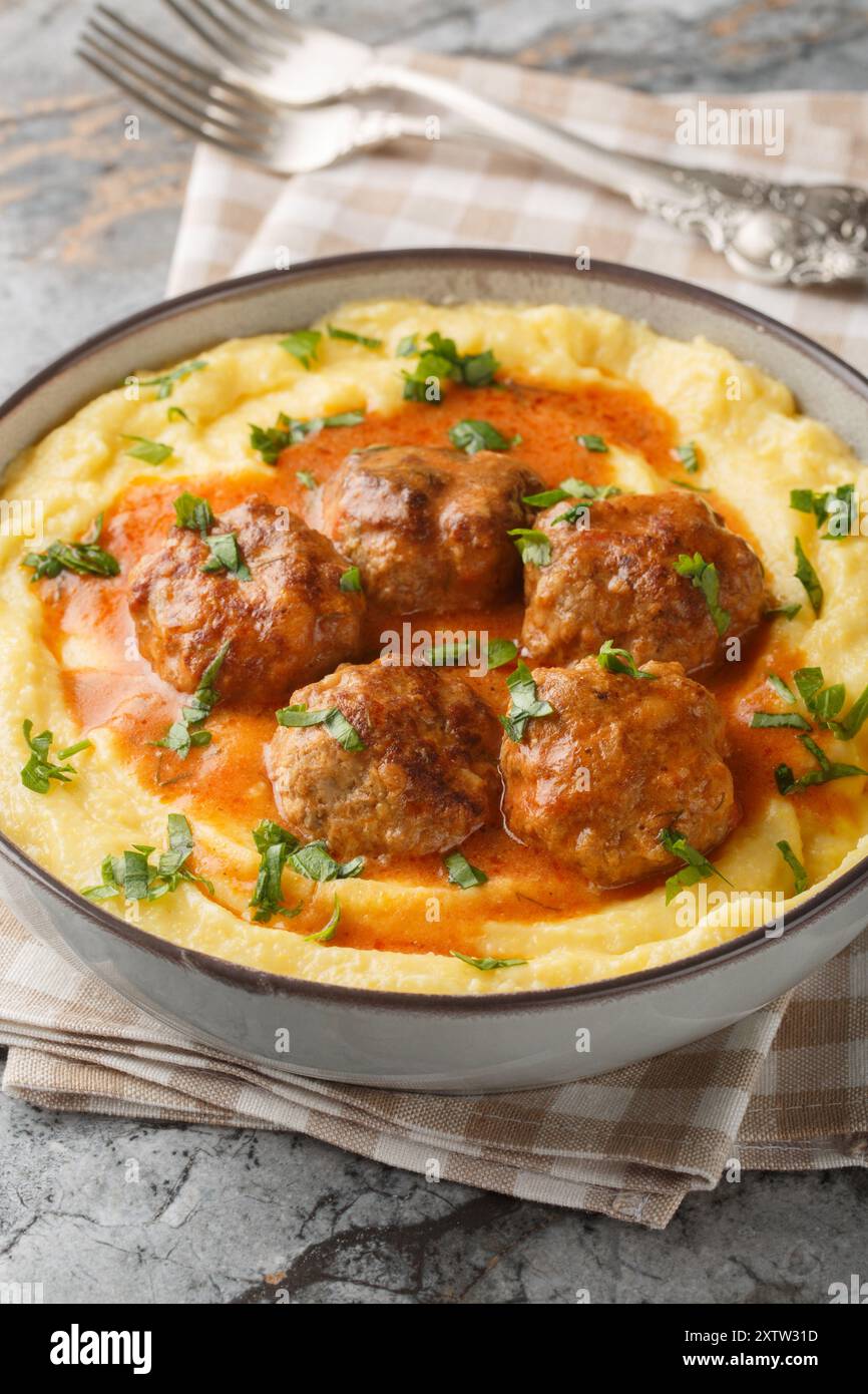 Polenta cremosa e polpette con primo piano sugo di carne sul recipiente sul tavolo. Verticale Foto Stock