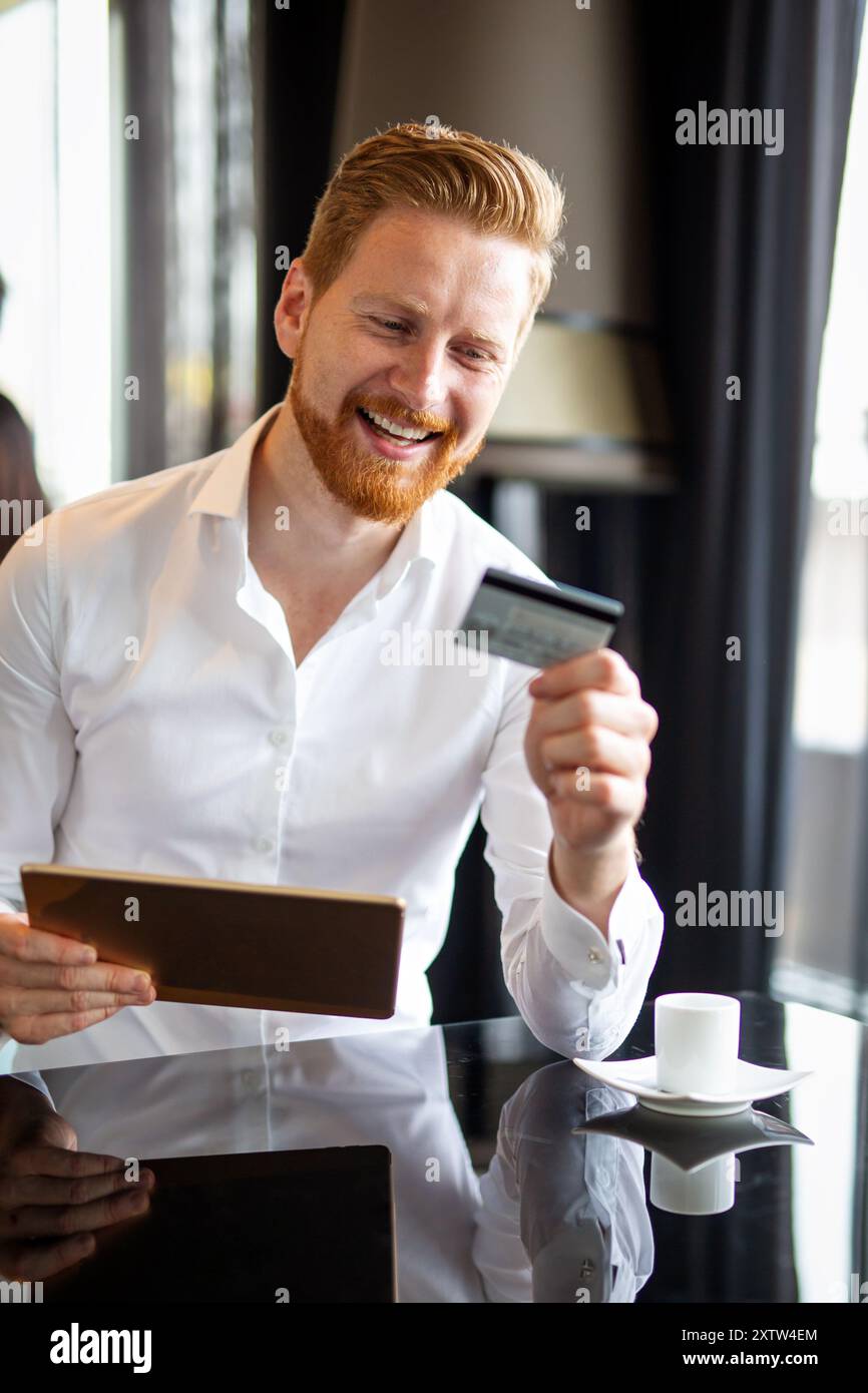 Uomo d'affari di successo che possiede una carta di credito, usando un tablet digitale. Concetto di shopping online Foto Stock