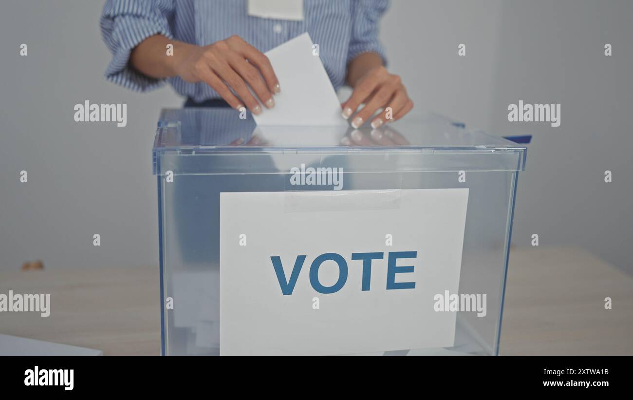 Una giovane donna getta il suo voto in una casella di voto libera in un centro elettorale al chiuso. Foto Stock