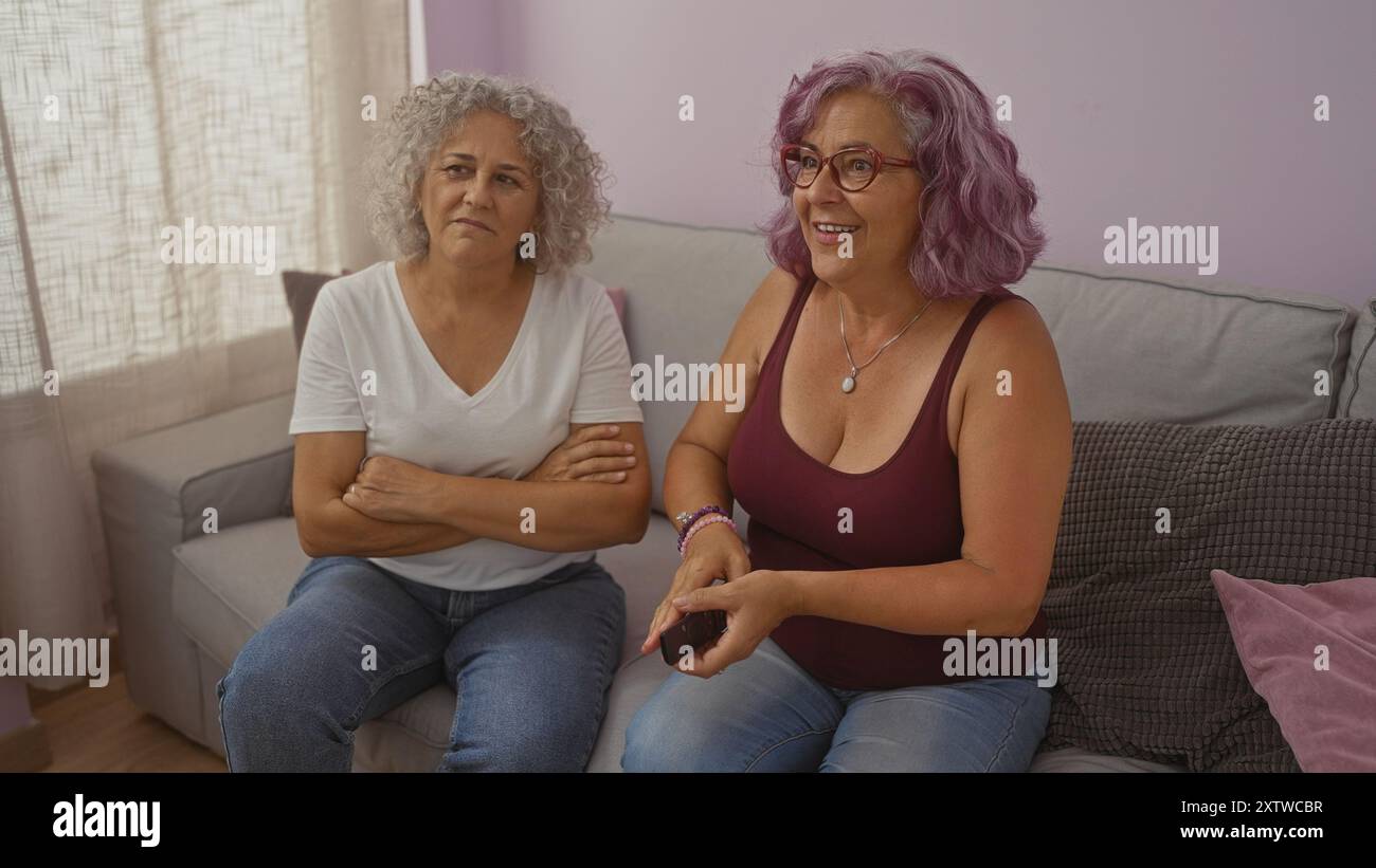 Due donne di mezza età con diverse acconciature si siedono insieme in un accogliente soggiorno, creando un'atmosfera calda e accogliente. Foto Stock