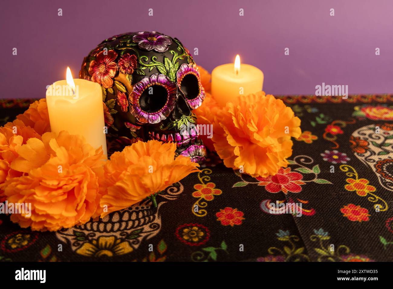 Un teschio decorato con fiori metallici, due candele che sfarfallio accanto ad esso. La scena è circondata da fiori d'arancio, mentre altre candele sono attentamente pla Foto Stock