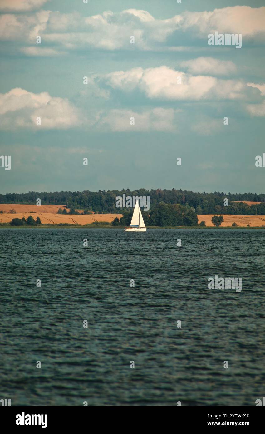 Solitaria barca a vela sul tranquillo lago con campi dorati in lontananza Foto Stock