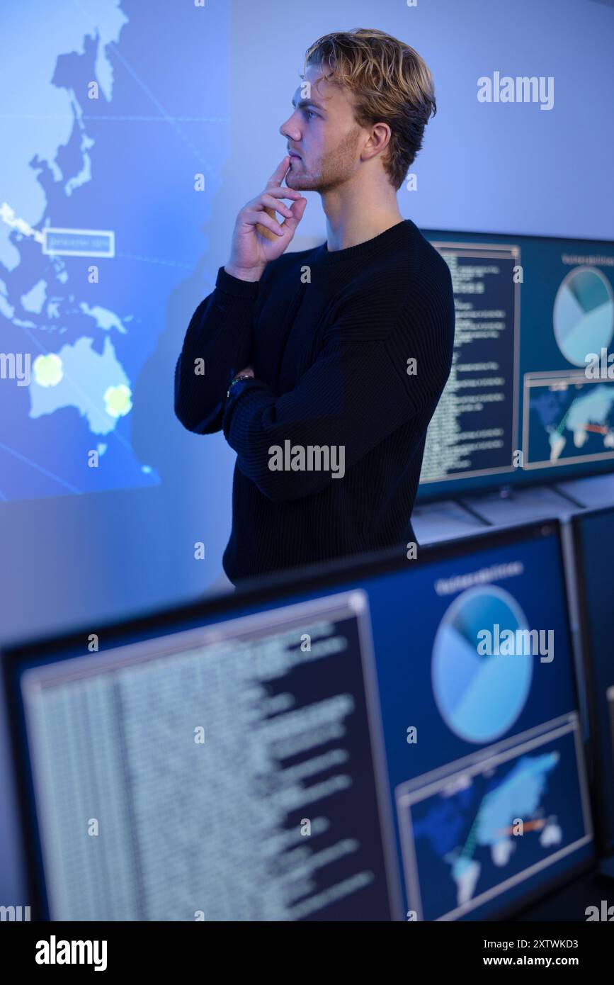 Un operatore attento e attento al Cyber Security Control Center. Più schermate che mostrano dati tecnici e avvisi. Foto Stock