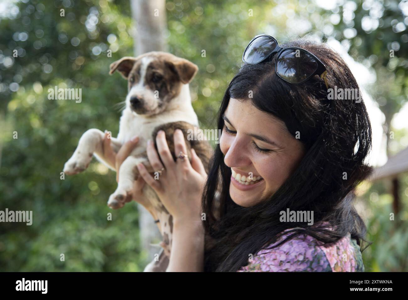 Donna sorridente che tiene un cucciolo giocoso all'aperto con alberi sullo sfondo. Foto Stock