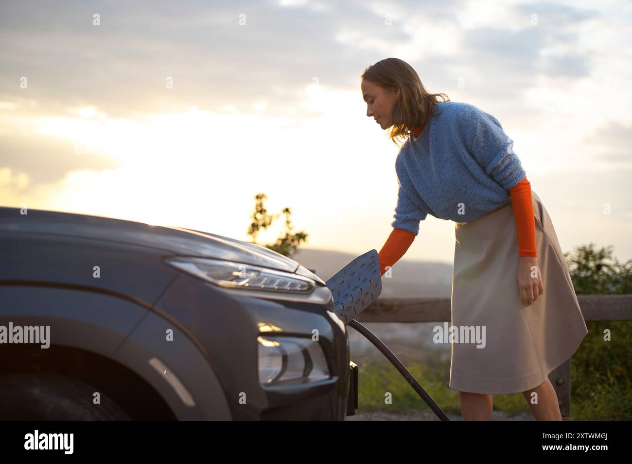 Donna che indossa un maglione che pulisce il faro di un'auto con un panno al tramonto. Foto Stock