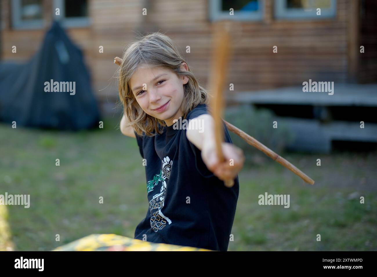 Bambino sorridente che si allontana con un bastone di legno in un giardino. Foto Stock