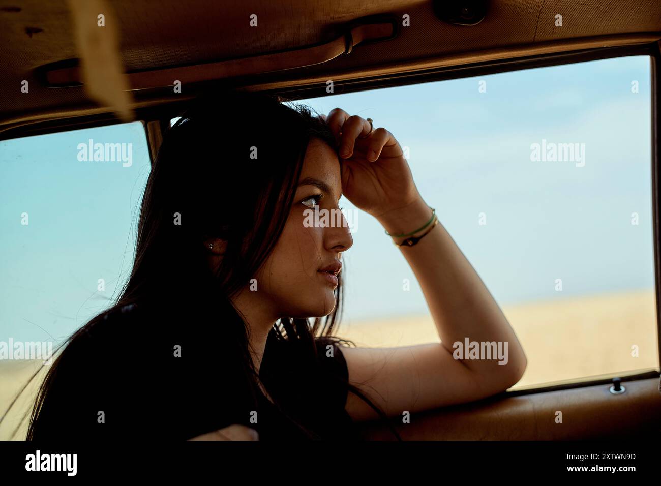Una giovane donna pensiva che guarda fuori dal finestrino di un'auto con uno sguardo lontano, la mano poggia sulla fronte. Foto Stock