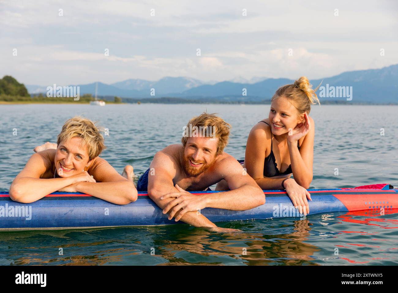 Tre amici che si godono una giornata di sole su una zattera gonfiabile in un lago con montagne sullo sfondo. Foto Stock
