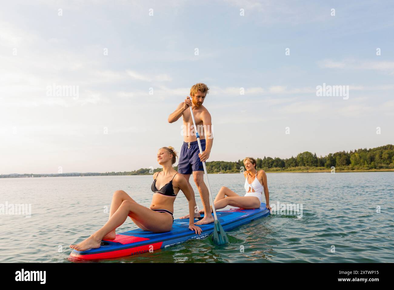 Gruppo di amici che si godono una giornata di sole in paddleboard sulle calme acque del lago. Foto Stock