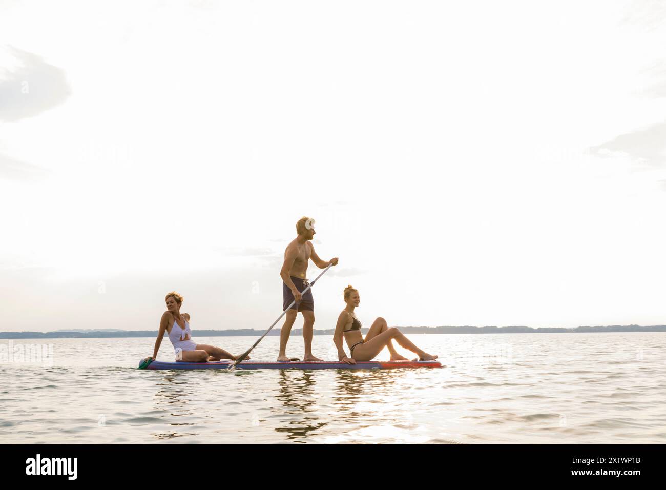 Tre amici si divertono a fare paddleboard su un lago tranquillo durante il tramonto. Foto Stock